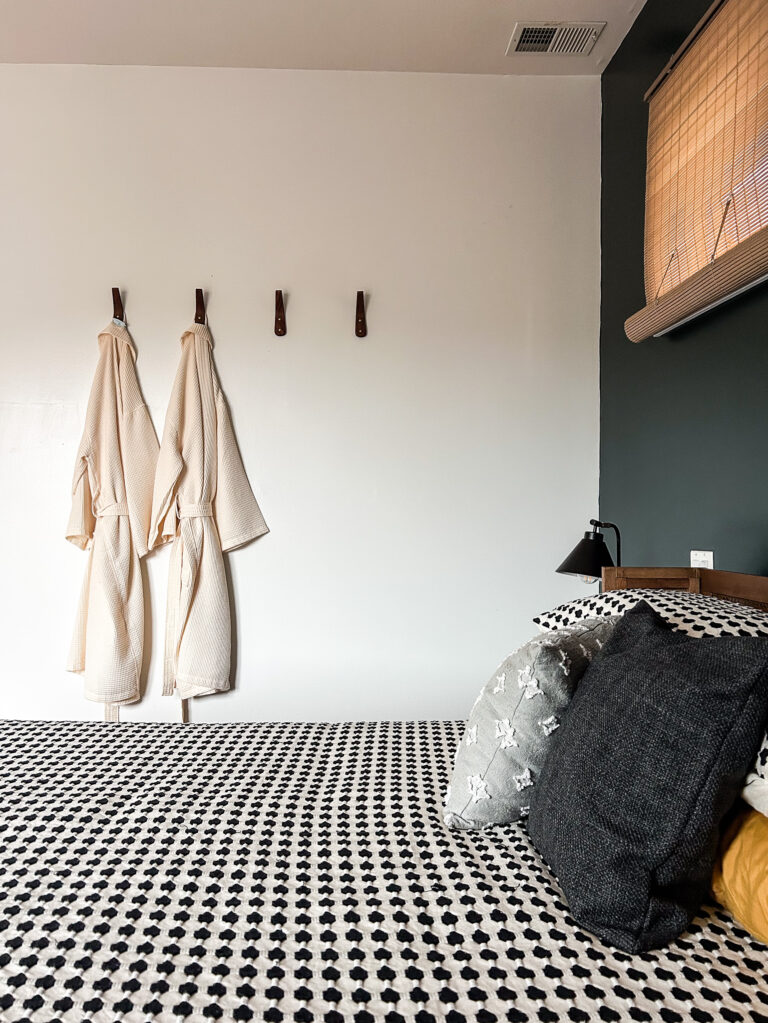 Clifton Condo bedroom featuring wall hooks, layered bedding, and moody green accents.