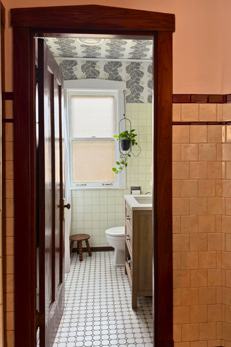 Renovated Bernard bathroom with vintage cream tile, patterned wallpaper ceiling, wood vanity, and black fixtures.