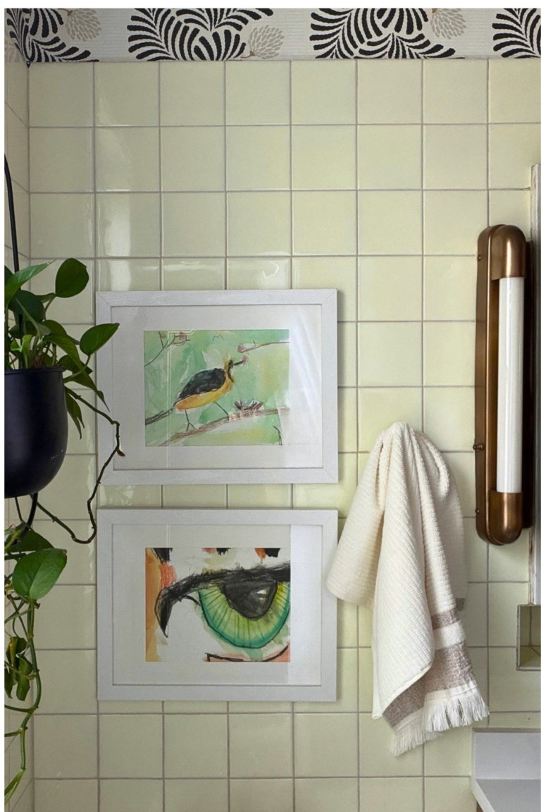 Bathroom sconce detail with brass vanity lighting, original cream tile walls, botanical wallpaper, and modern black faucet.