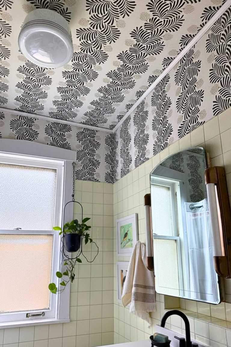 Historic bathroom with black and white botanical wallpaper ceiling, original cream wall tile, and vintage light fixture.