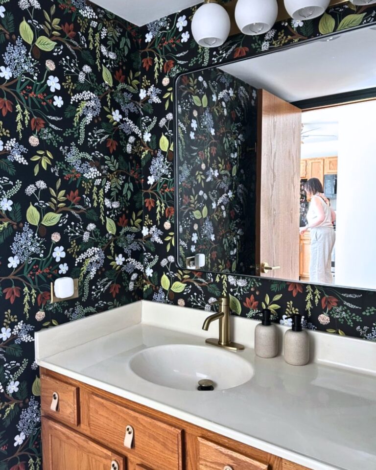 Essex Bath bathroom renovation with dark botanical wallpaper, brass faucet, white countertop, and oak vanity